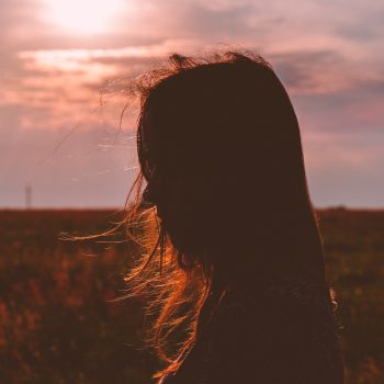 Silhouette junger Frau mit wehenden Haaren vor offenem Feld