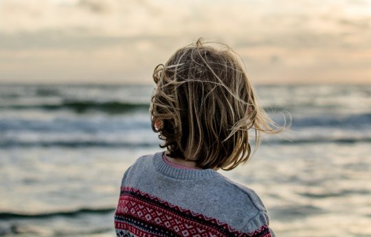 junge Person von hinten blickt auf Meer hinaus bei Sonnenaufgang